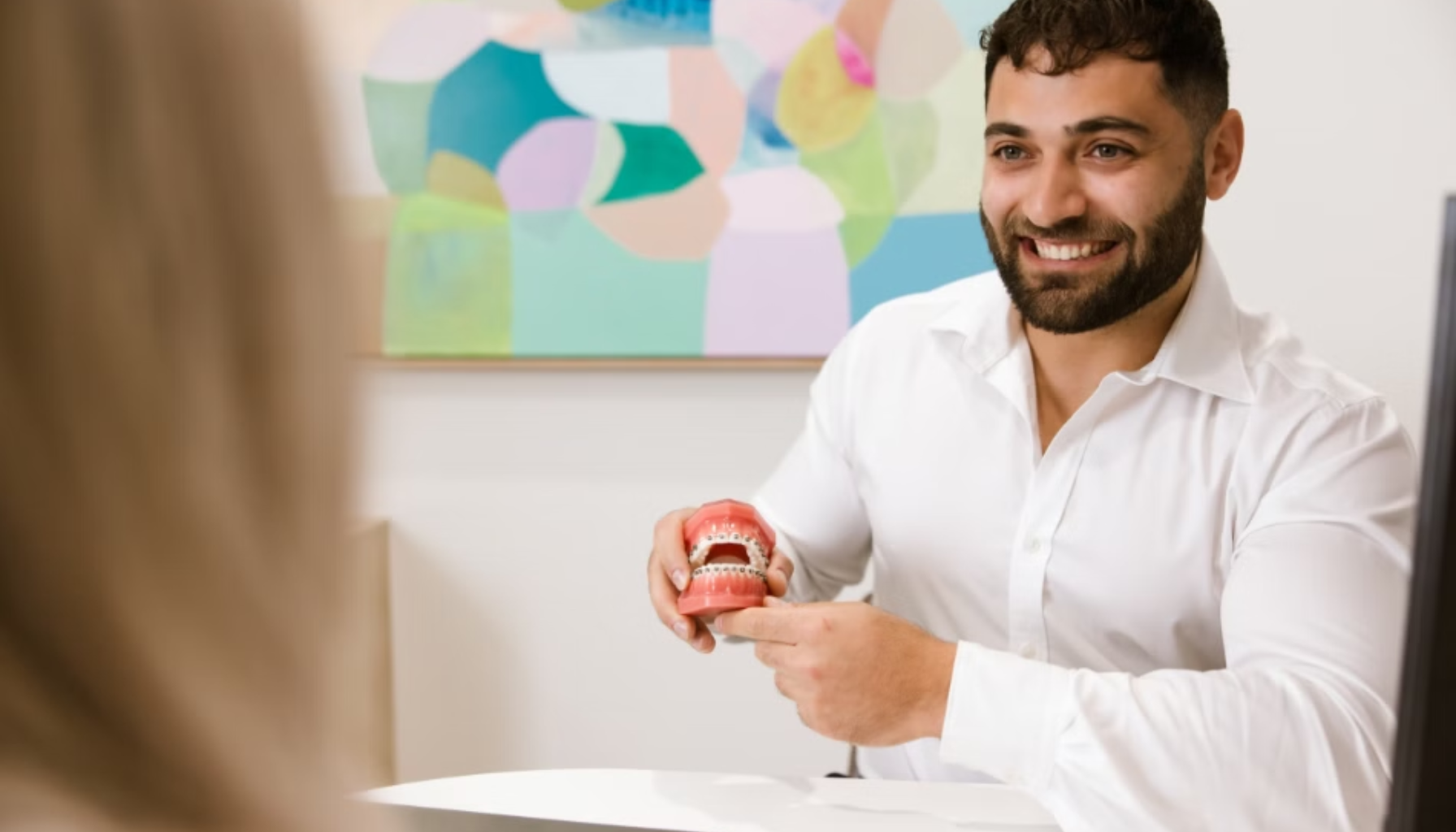 Skjeve tenner: Når estetikk og tannhelse henger sammen 12 Smilende tannlege viser pasient en tannmodell med regulering under konsultasjon på et lyst og moderne kontor.