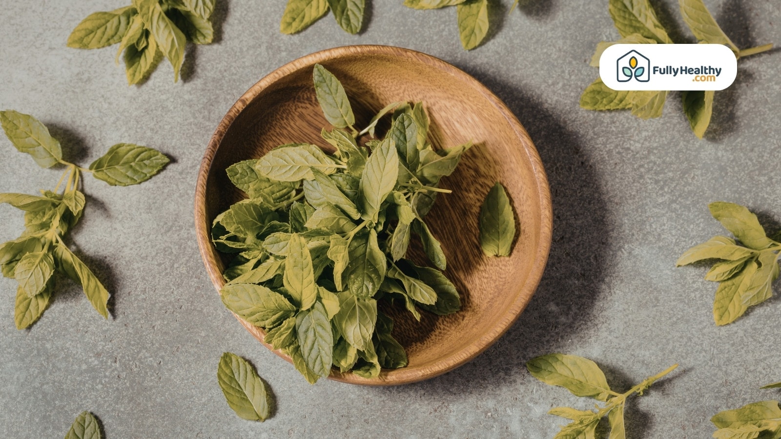 Fresh oregano leaves in wooden bowl with scattered leaves around