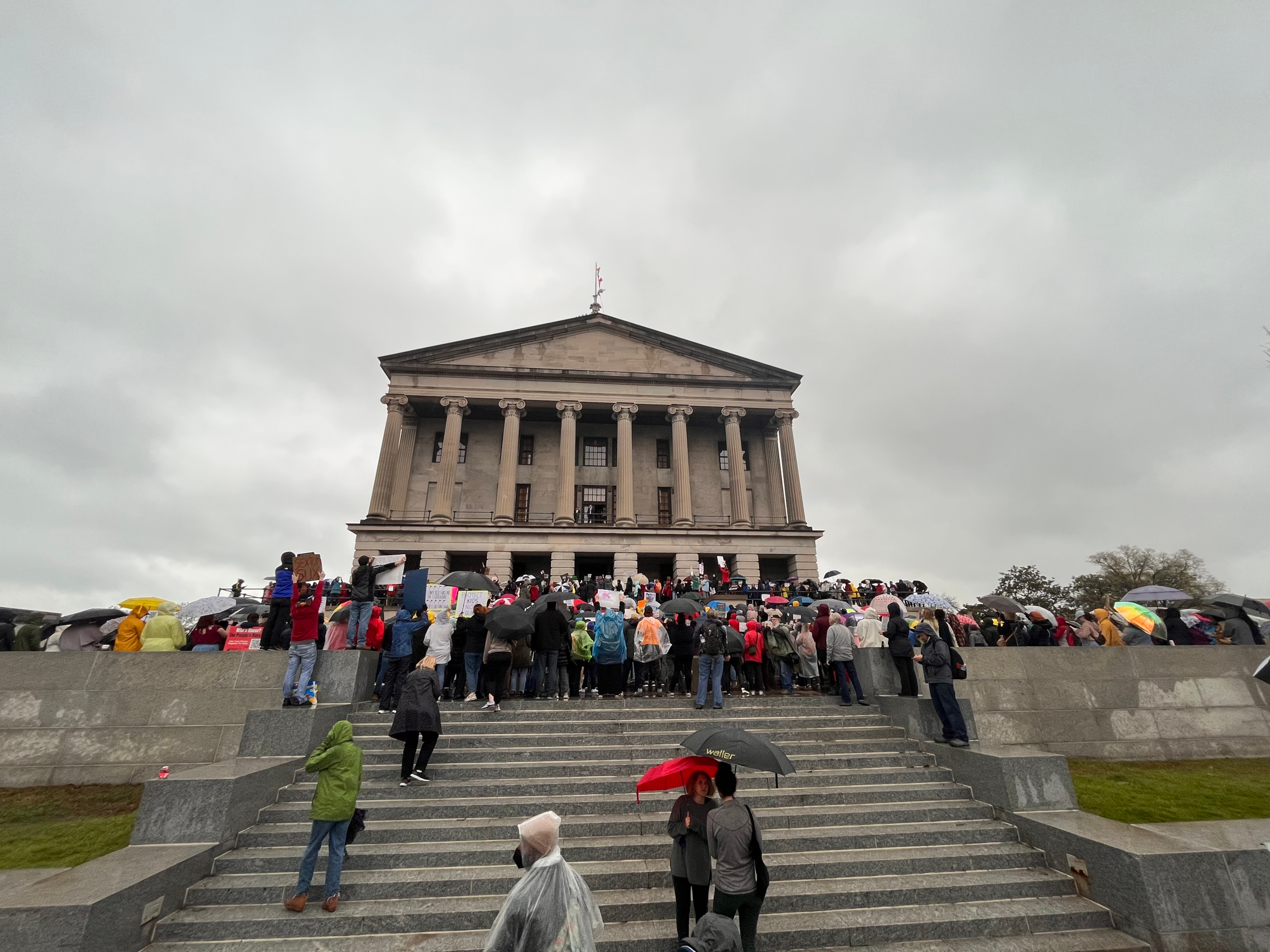 Crowd with umbrellas in front of official building on a rainy day.