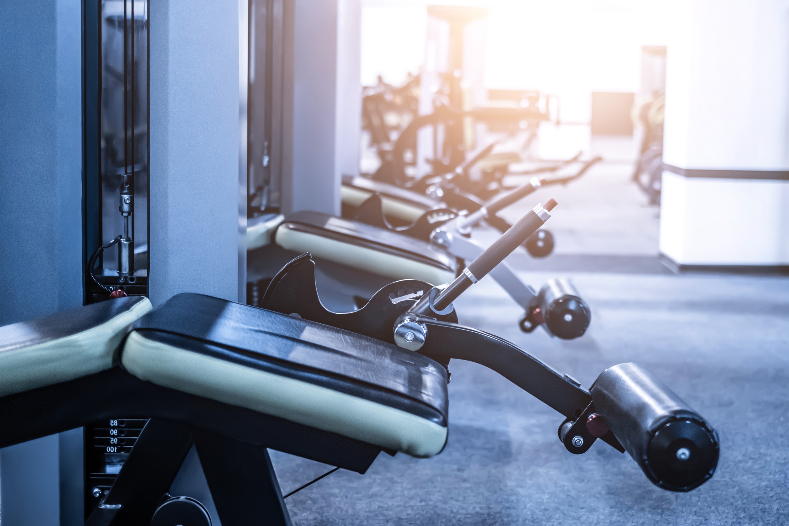 A row of leg and hamstring trainers sitting empty in a gym