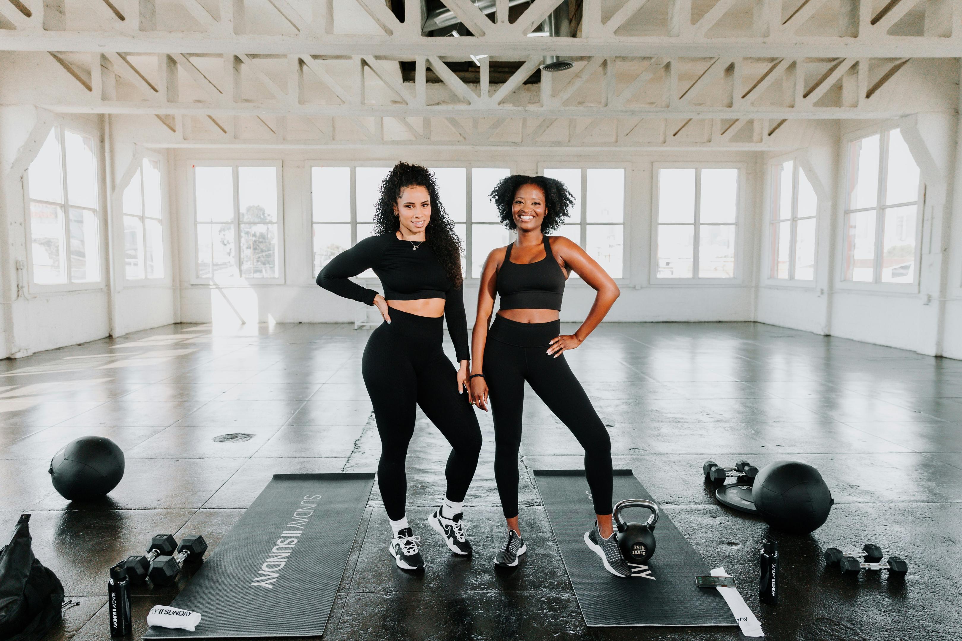 two women, in exercise gear in a gym, about to workout
