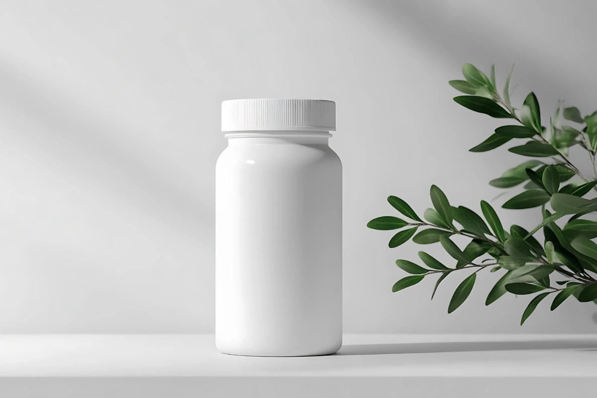 A white bottle sits on a shelf next to a branch with green leaves.