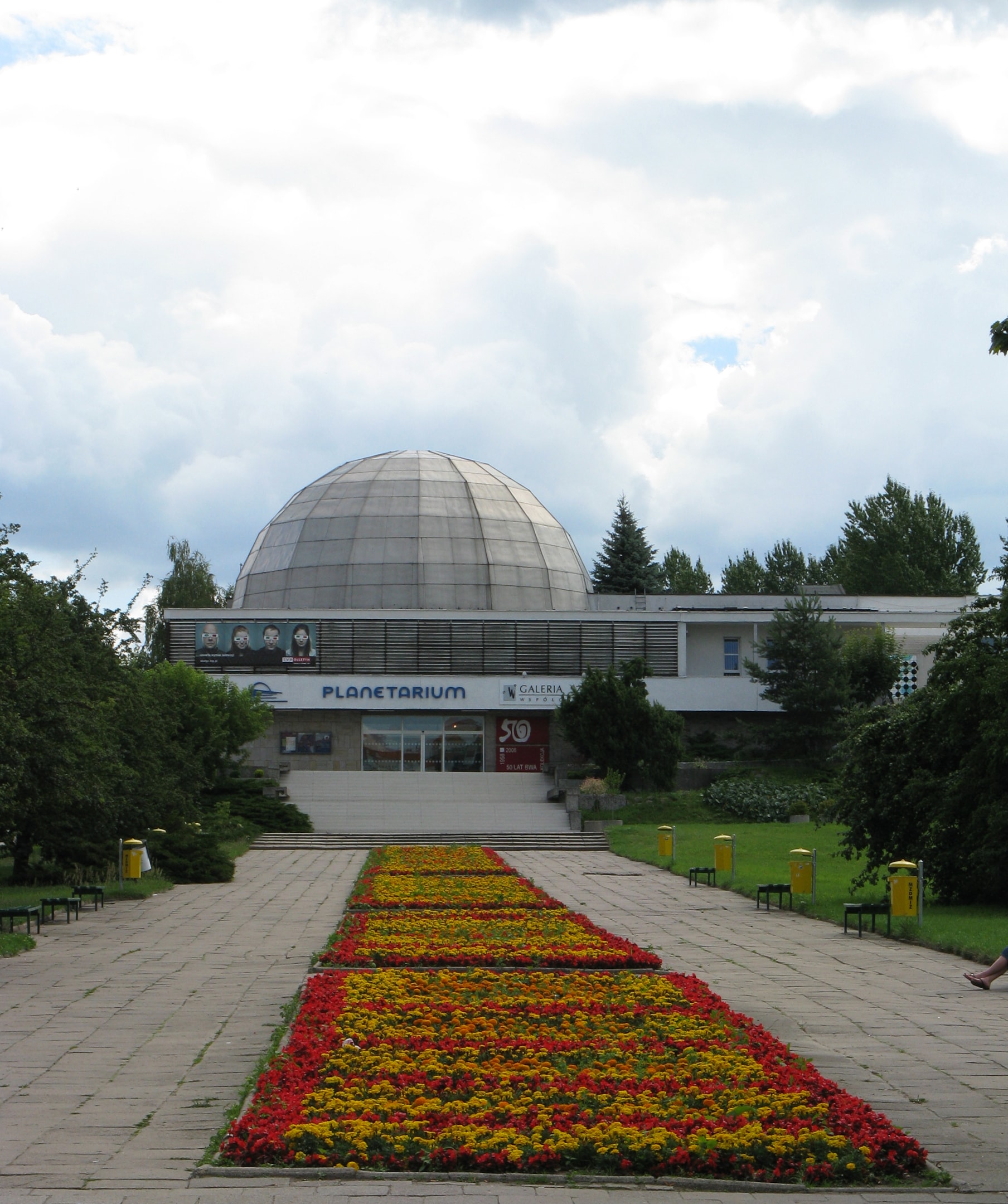 W samym Olsztynie można podziwiać cały kosmos za sprawą Olsztyńskiego Planetarium, które widać na zdjęciu. Budynek ma imponującą kopułę, a przed jego wejściem rozciąga się dywan kwiatowy. Źródło: https://commons.wikimedia.org/wiki/File:Planetarium_w_Olsztynie.jpg