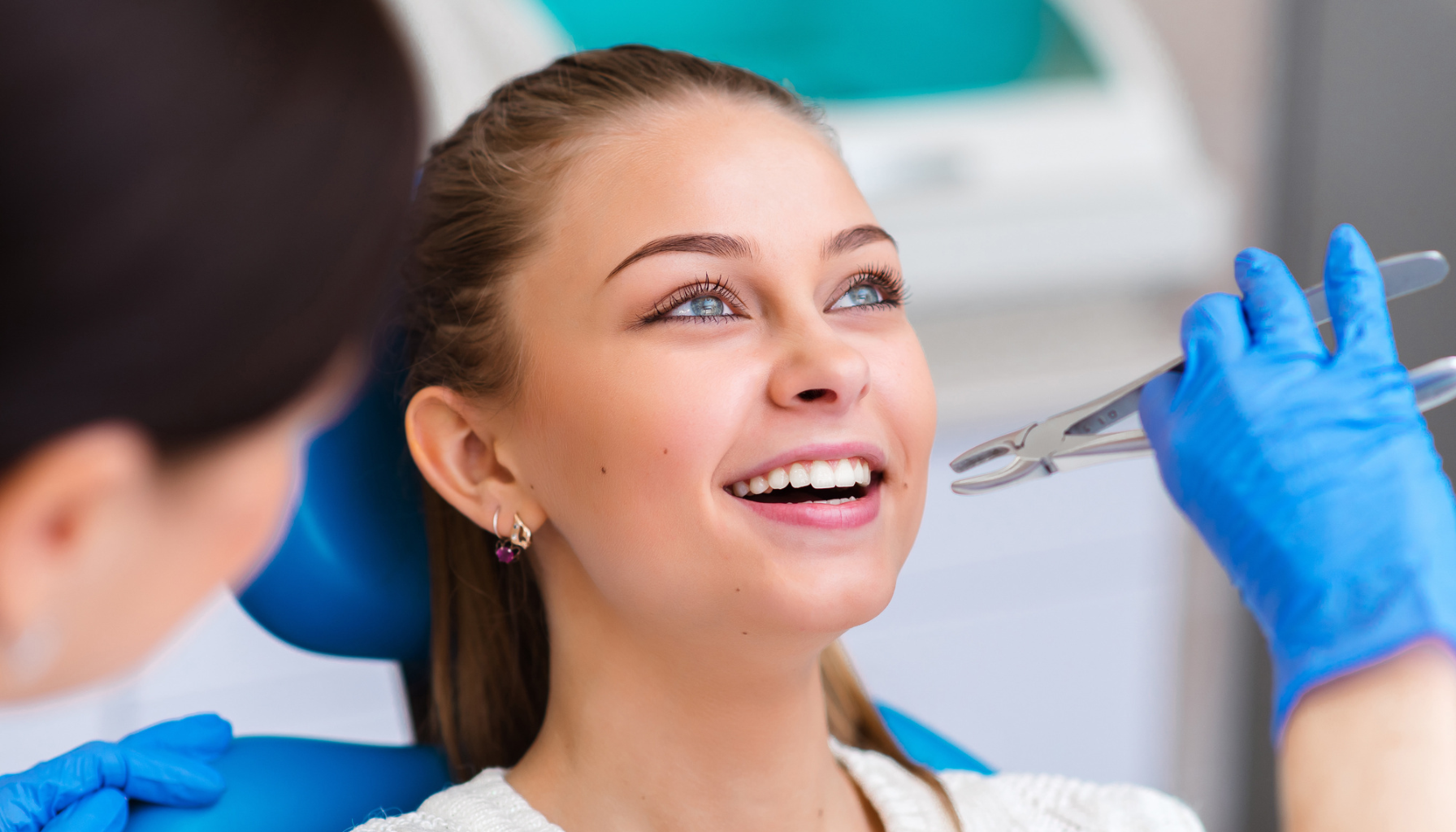 Ung kvinne smiler hos tannlegen før en tannbehandling med tang. Tannpleier med hansker gjør klar til prosedyre i klinisk miljø.