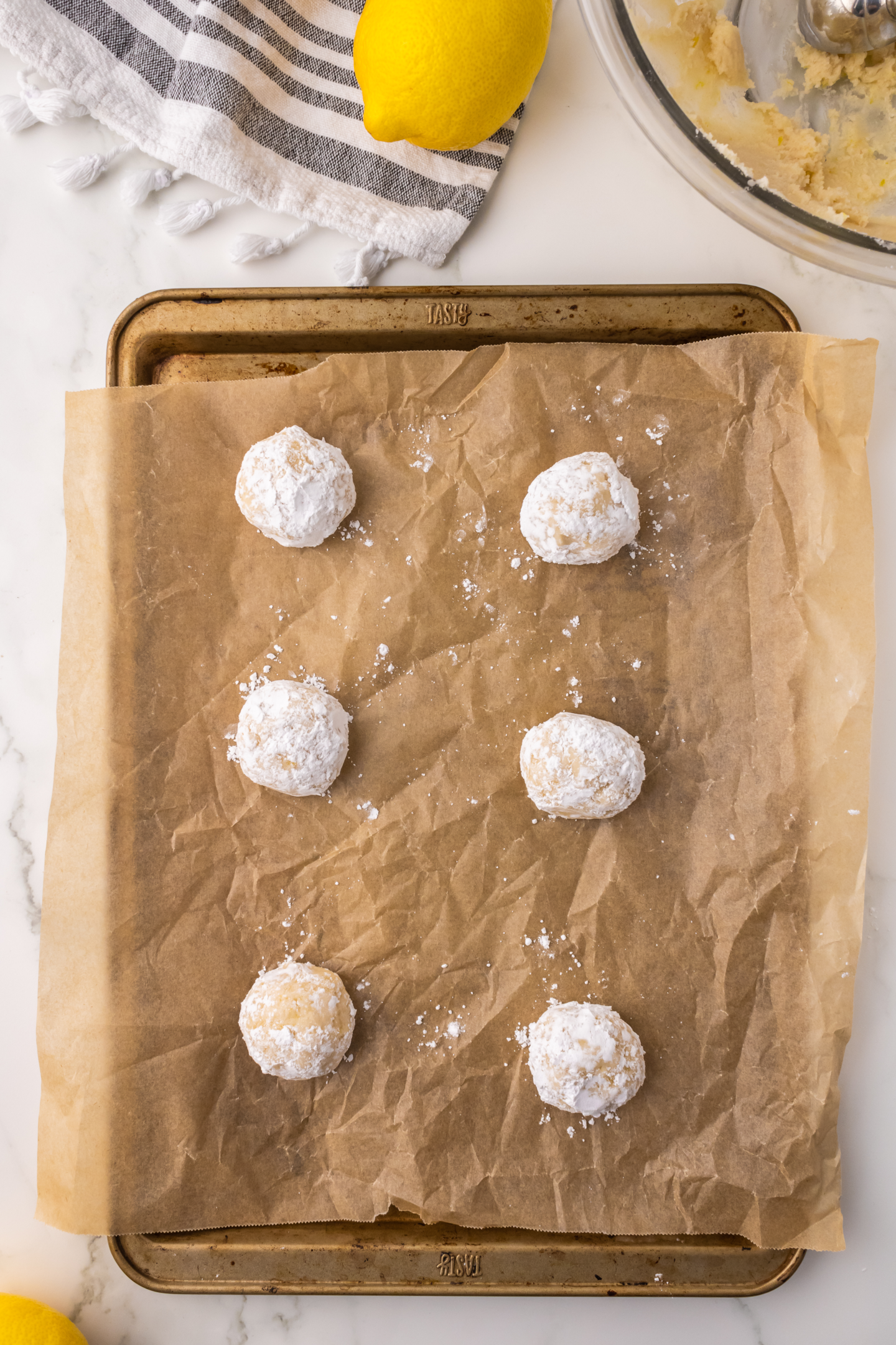 six unbaked lemon crinkle cookies rolled in powdered sugar on baking sheet