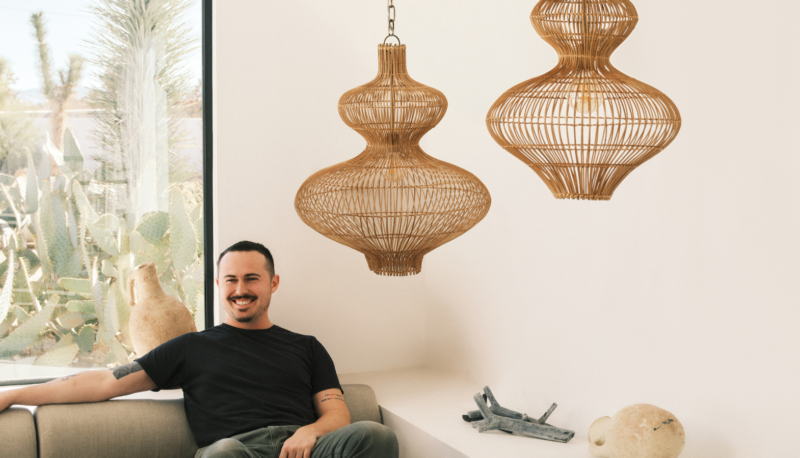 Chandler McLellan sitting beneath two woven pendant lights from his Troy Lighting collection.