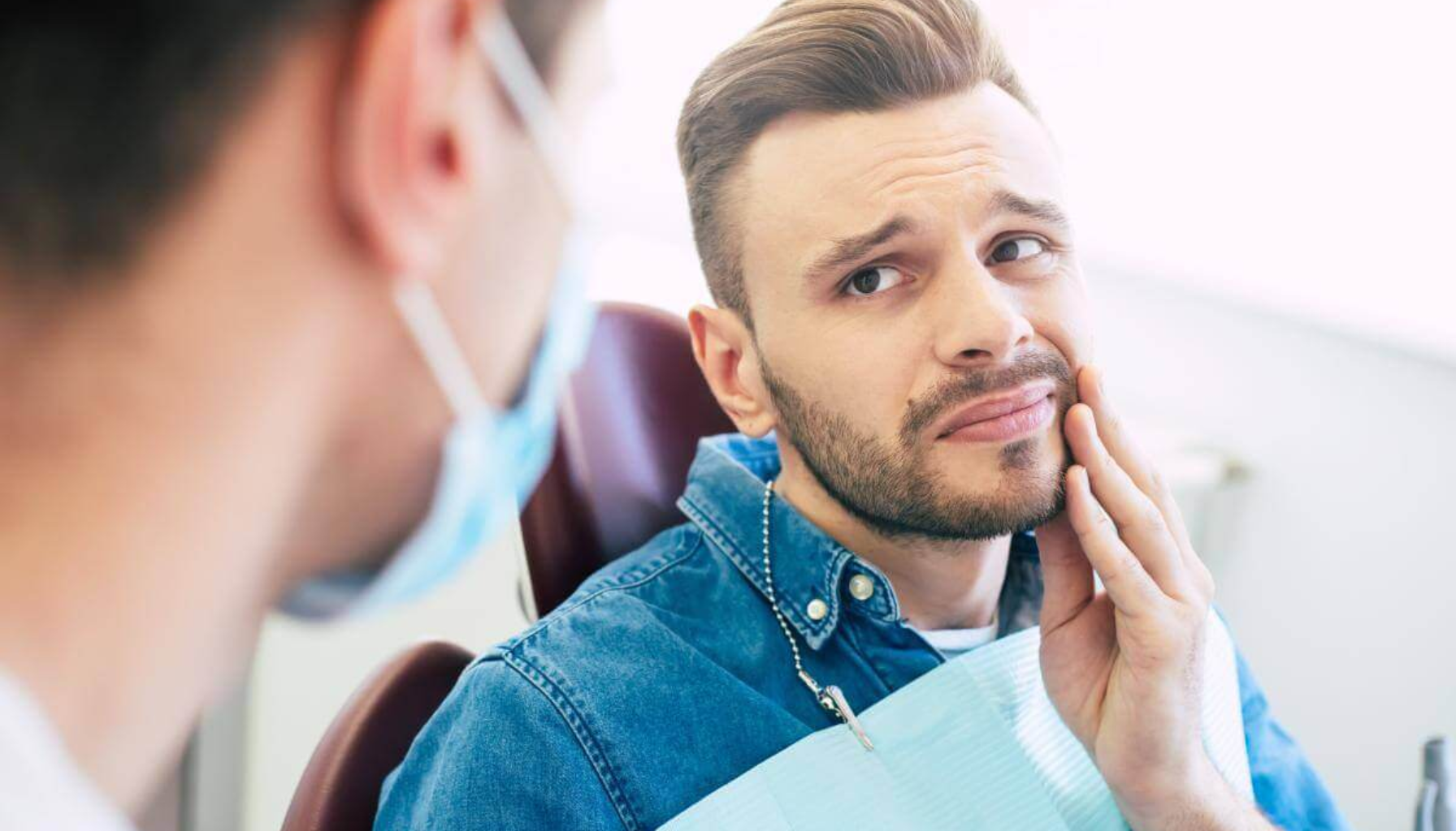 Mann hos tannlege holder seg til kinnet og ser bekymret ut på grunn av tannpine eller ubehag i munnen. behandling av helvetesild varicella zoster virus løpet av livet vaksine mot helvetesild side av kroppen helvetesild i løpet antivirale legemidler avgrenset hudområde sm hos eldreertefullt utslett levende svekket zoster ophthalmicus 60 år virus symptomer dager kroppen vaksiner øyet