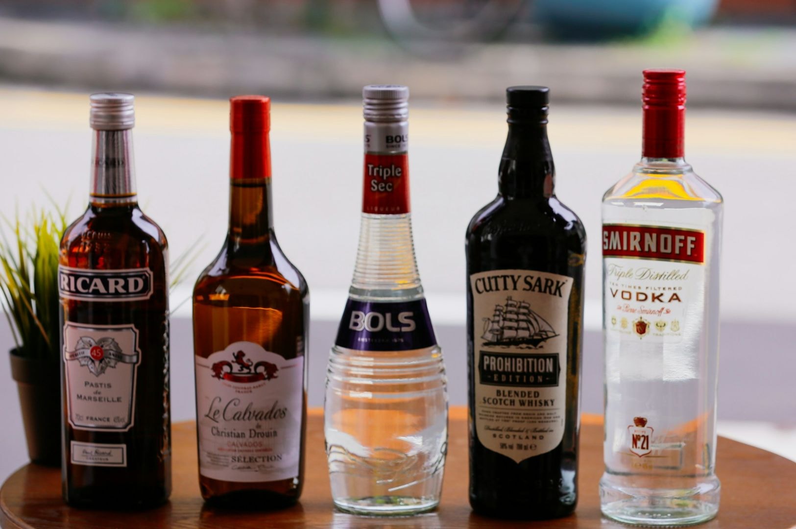 Five liquor bottles are lined up on a wooden surface. They vary in color and design, set against a blurred background, evoking a casual atmosphere.