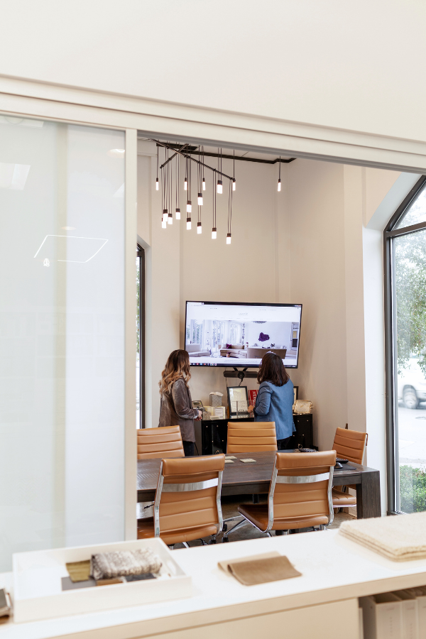 Two designers standing in a small presentation room, reviewing images on a large screen.