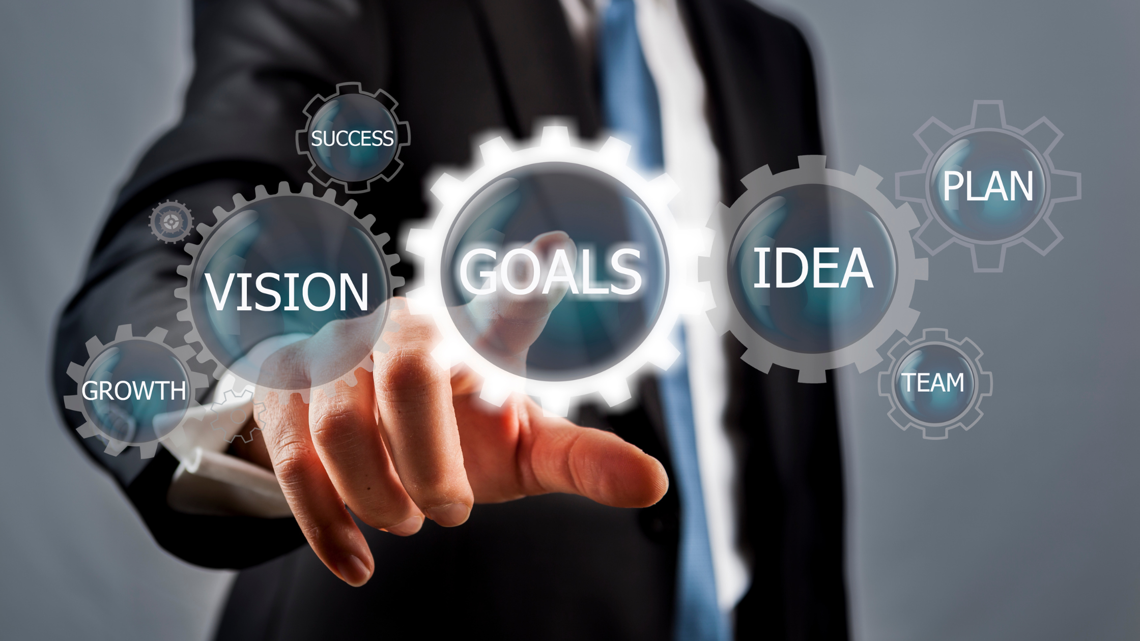 A businessman interacting with holographic gears labeled 'Vision,' 'Goals,' 'Plan,' and 'Growth,' highlighting strategic planning and teamwork.