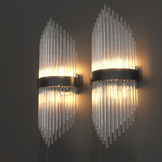 Pair of modern wall sconces with vertically aligned glass rods forming a diamond-shaped design, featuring a central black metal band. The lights emit a warm glow through the glass, creating an elegant and contemporary look against a dark wall.