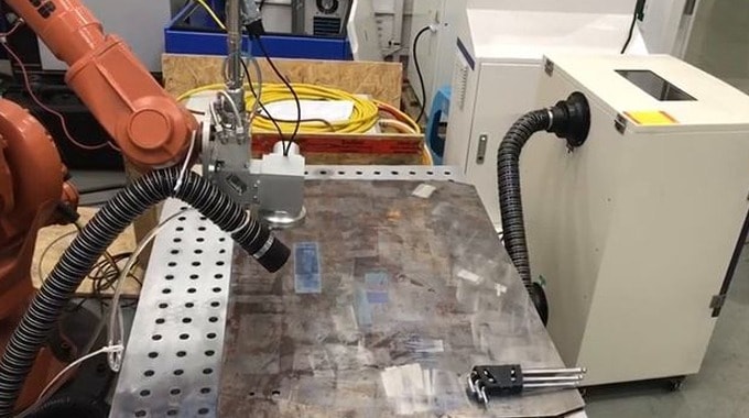 A laser cleaning head on a metal surface, connected to an extraction unit.