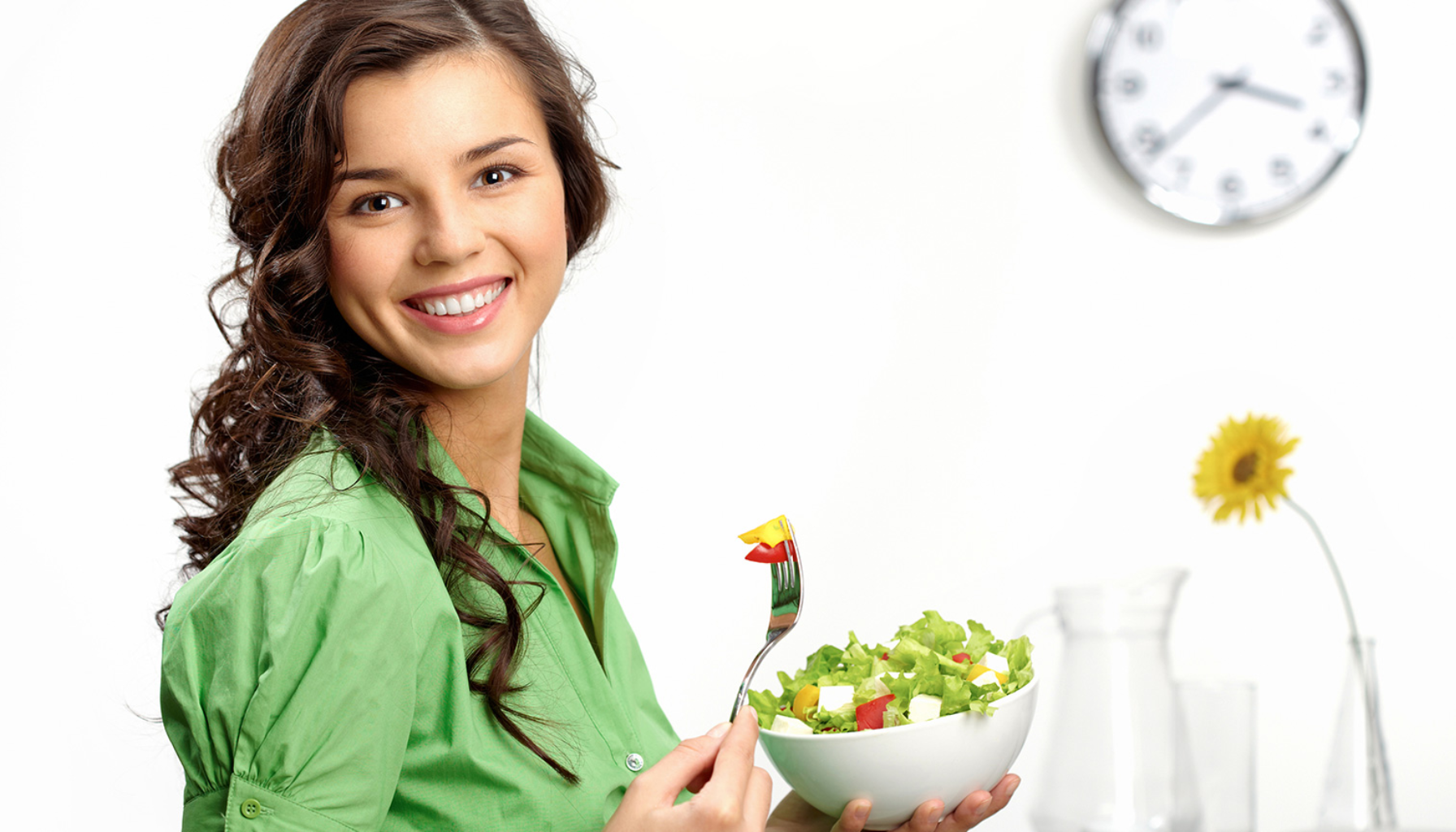 Spise Etter Tannlege: Hva Du Bør (og Ikke Bør) Gjøre Etter Behandling 11 Smilende kvinne i grønn skjorte spiser frisk salat med gaffel, symboliserer sunn livsstil og kosthold.