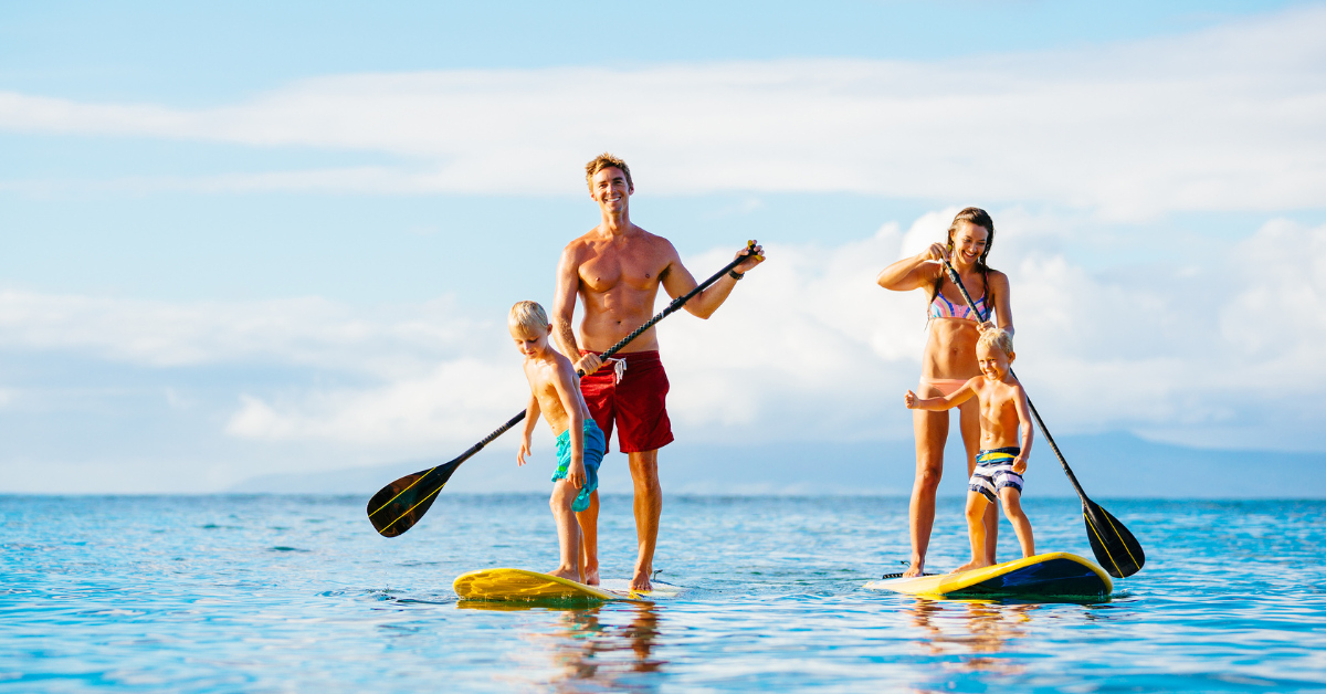 Family paddleboarding together on calm ocean waters near Cape May, enjoying a sunny day and coastal recreation during their beach vacation.
