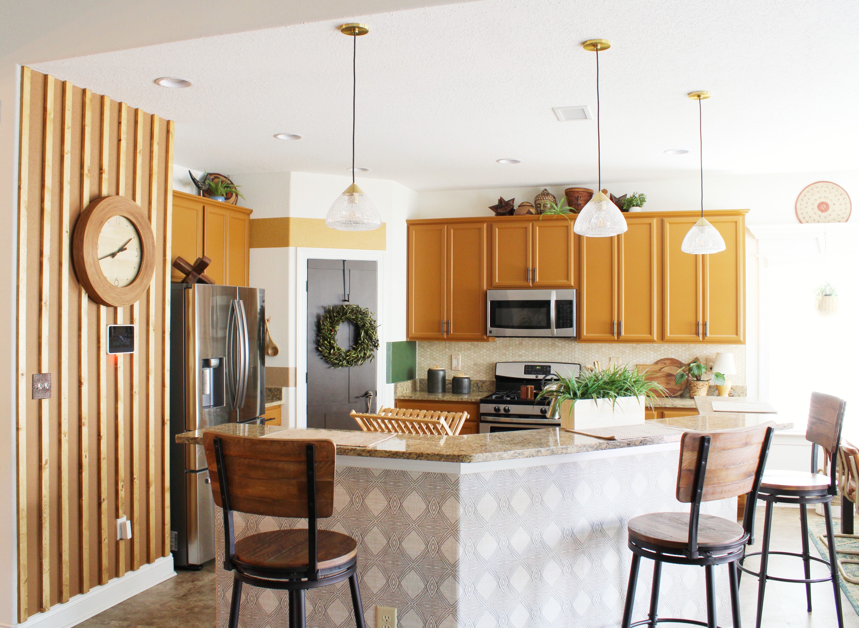 Light-filled kitchen with large white pendant lights over the island, festive wreaths, and wood accents for a modern holiday ambiance.