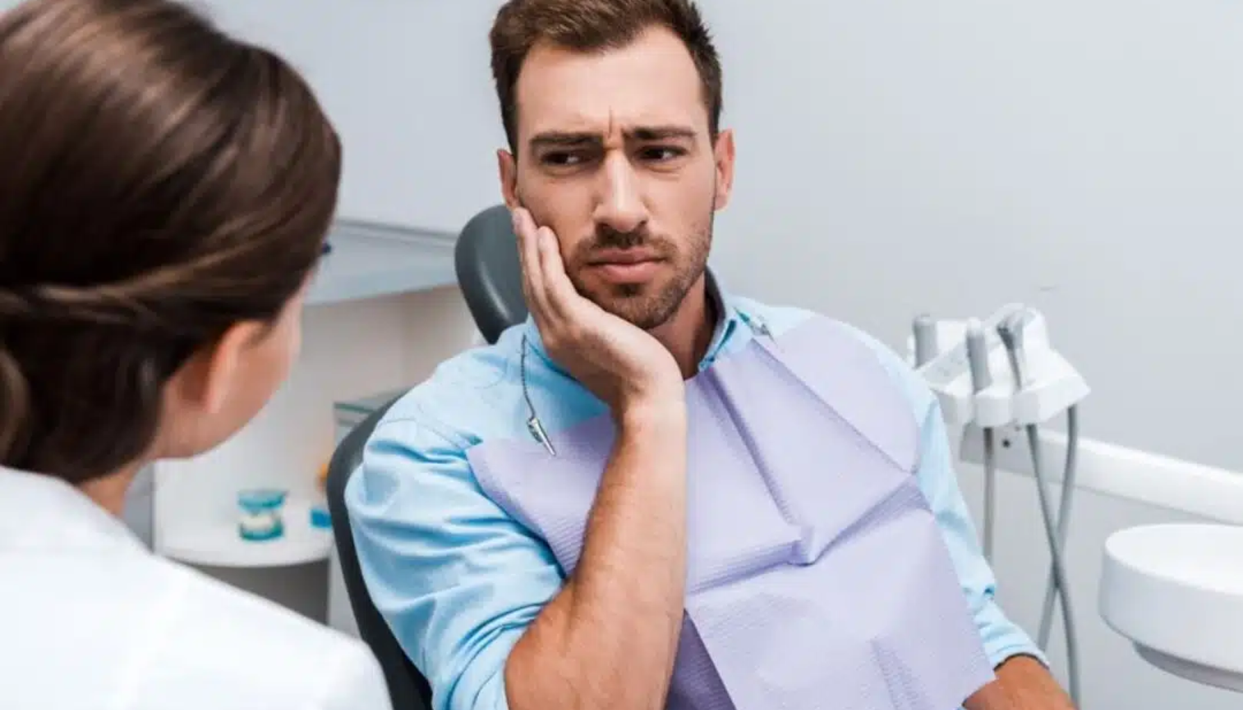 Smerter i hodet når du bøyer deg: tett forbindelse mellom bihuler og tannrøtter 15 Mann sitter i tannlegestol og holder kinnet mens han forklarer smerter til tannlege.