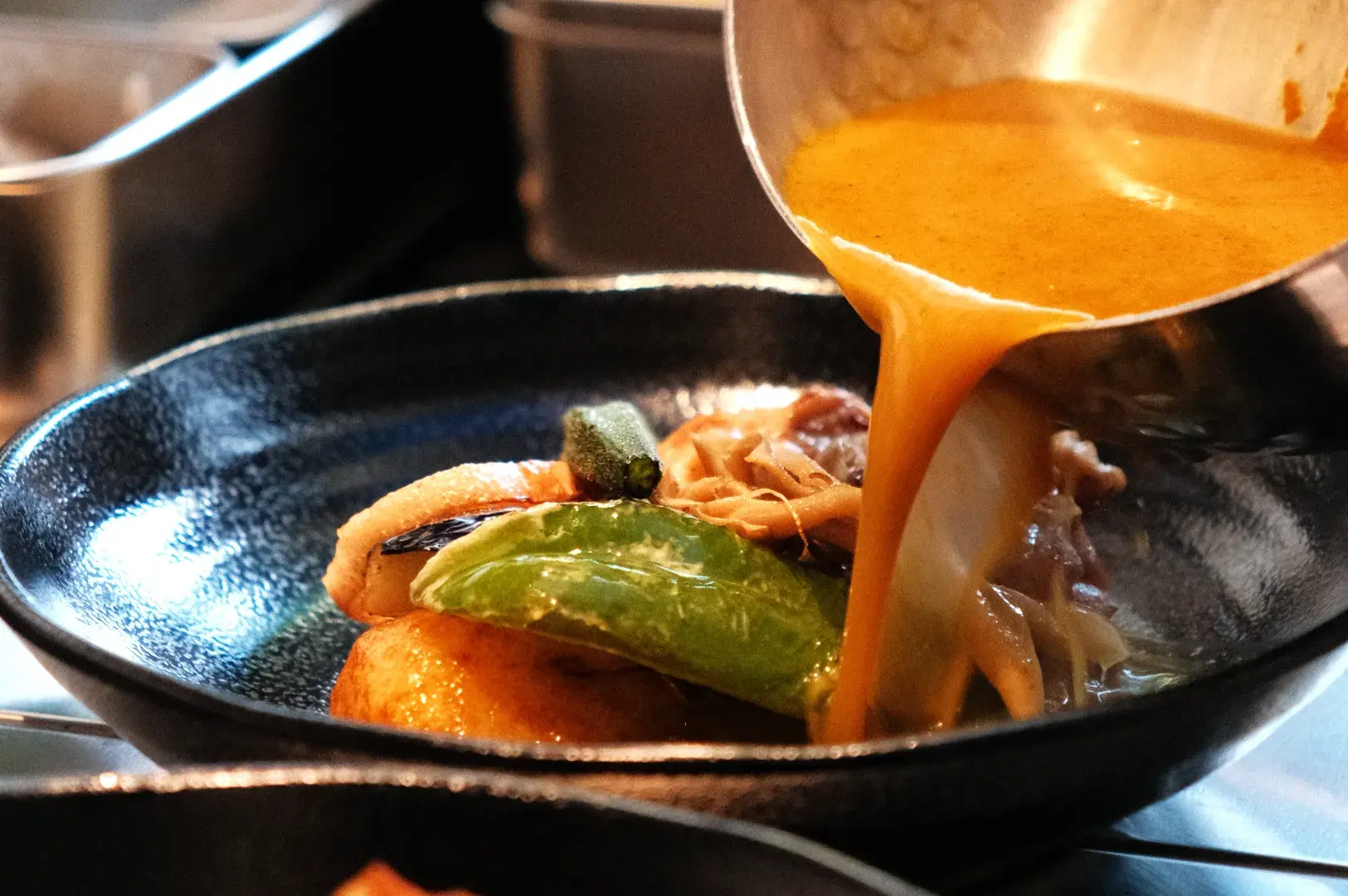 A chef pouring sauce over a plate of food with vegetables and proteins.