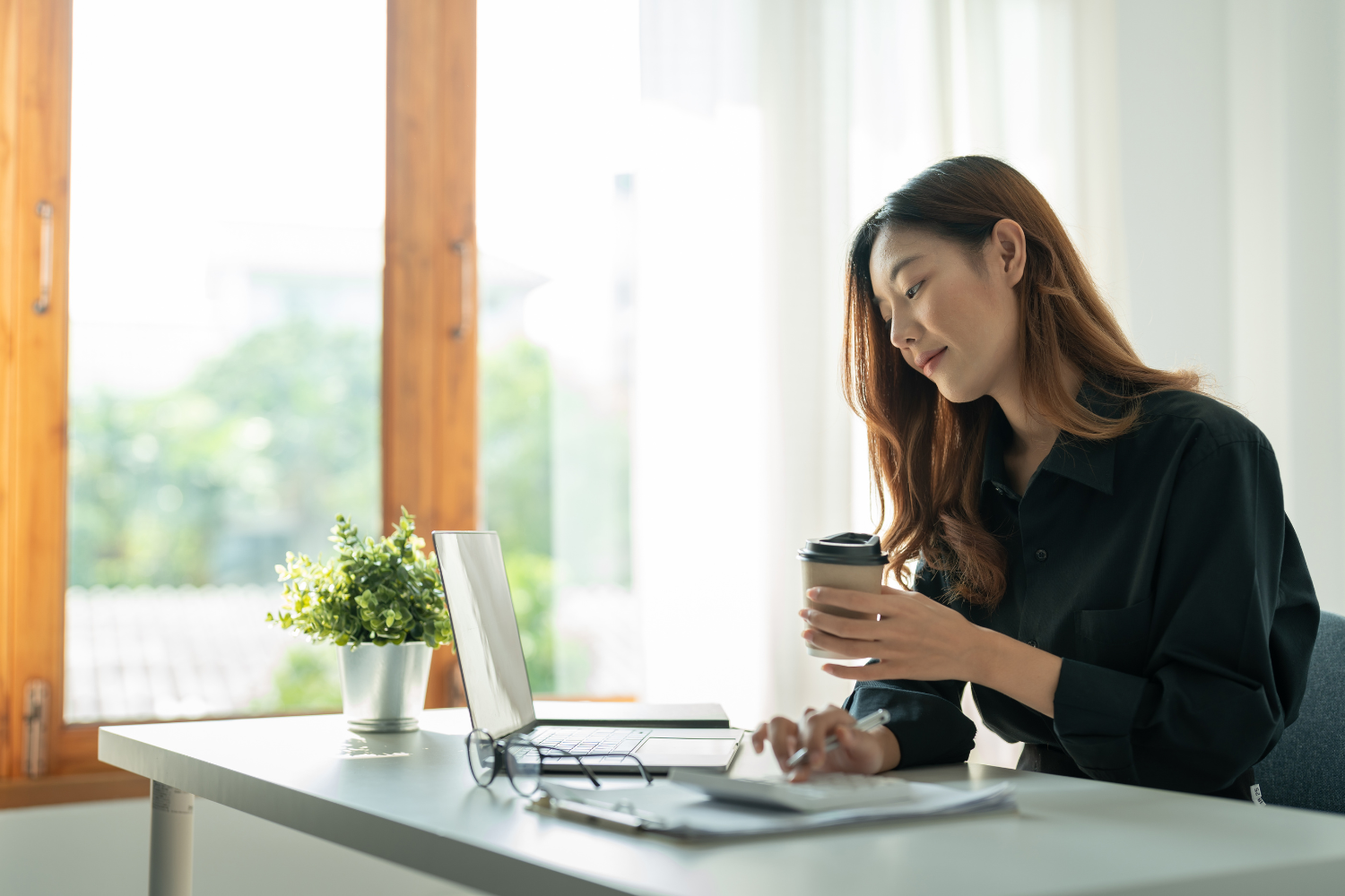 A small business owner reviewing something on her laptop while holding her take-out coffee.