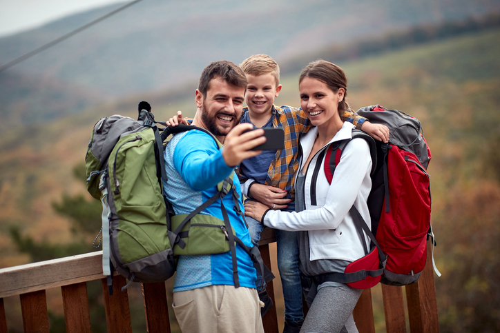 Happy young family of three snapping a selfie during a hike. 