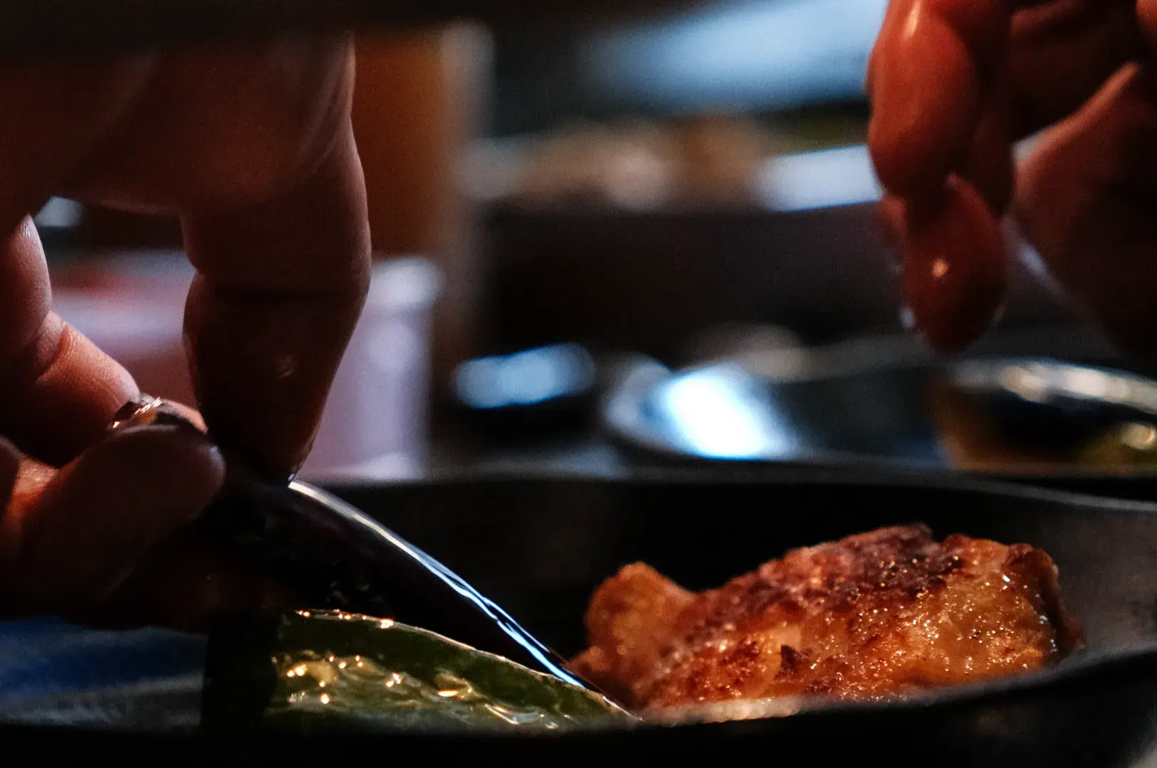 A close-up of hands delicately handling food on a plate, with one hand using a fork or utensil and the other hand reaching for a piece of food.