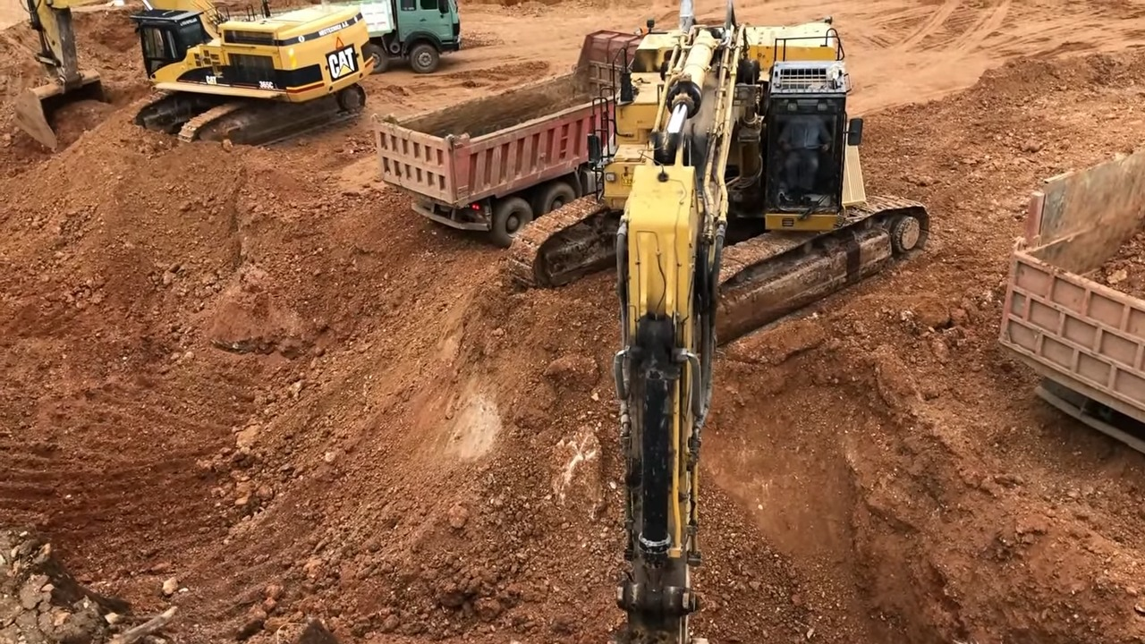 Several construction vehicles, including an excavator and dump trucks, working on a dirt-filled construction site