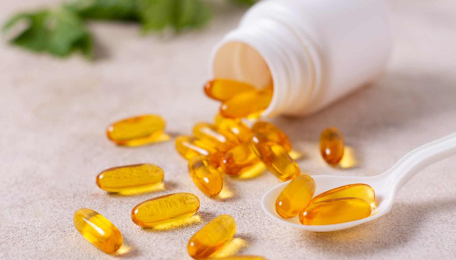 Vitamin D verdier – Hva er normalt og når bør du ta tilskudd? 17 Gule gelékapsler med kosttilskudd ligger spredt på bordet ved siden av en hvit plastflaske og skje.