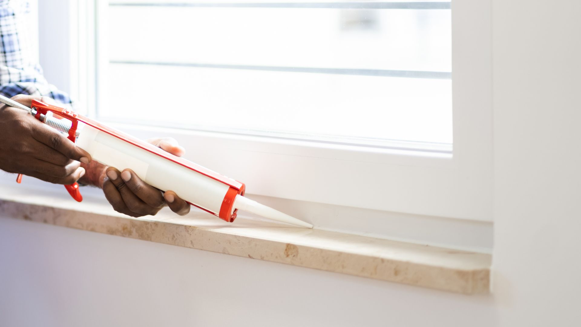 An image of a person using silicone latex caulk on their window frame to prevent bugs from entering. 