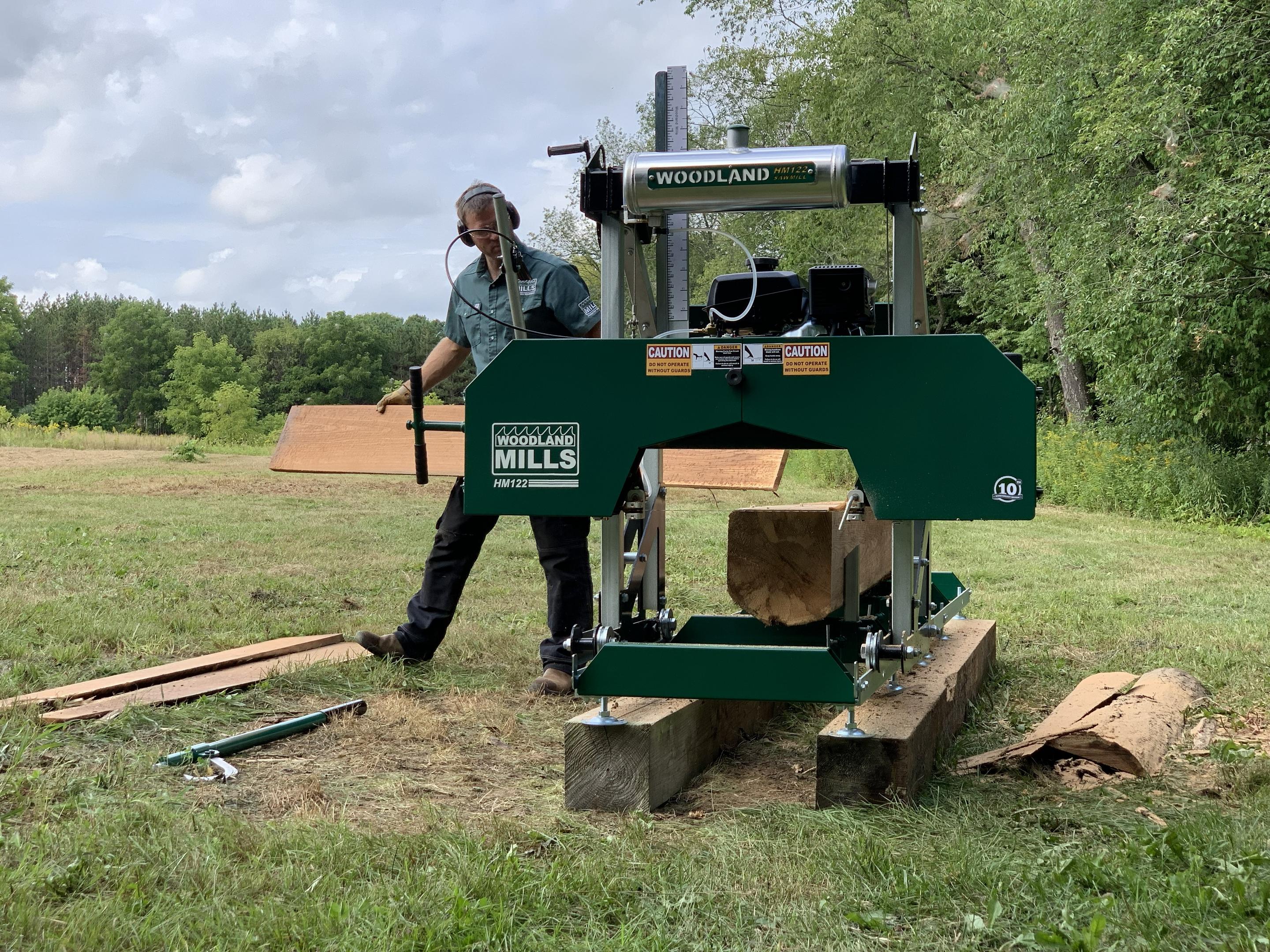 A man standing beside a Woodland Mills HM122 Portable Sawmill with a cant on the track. 