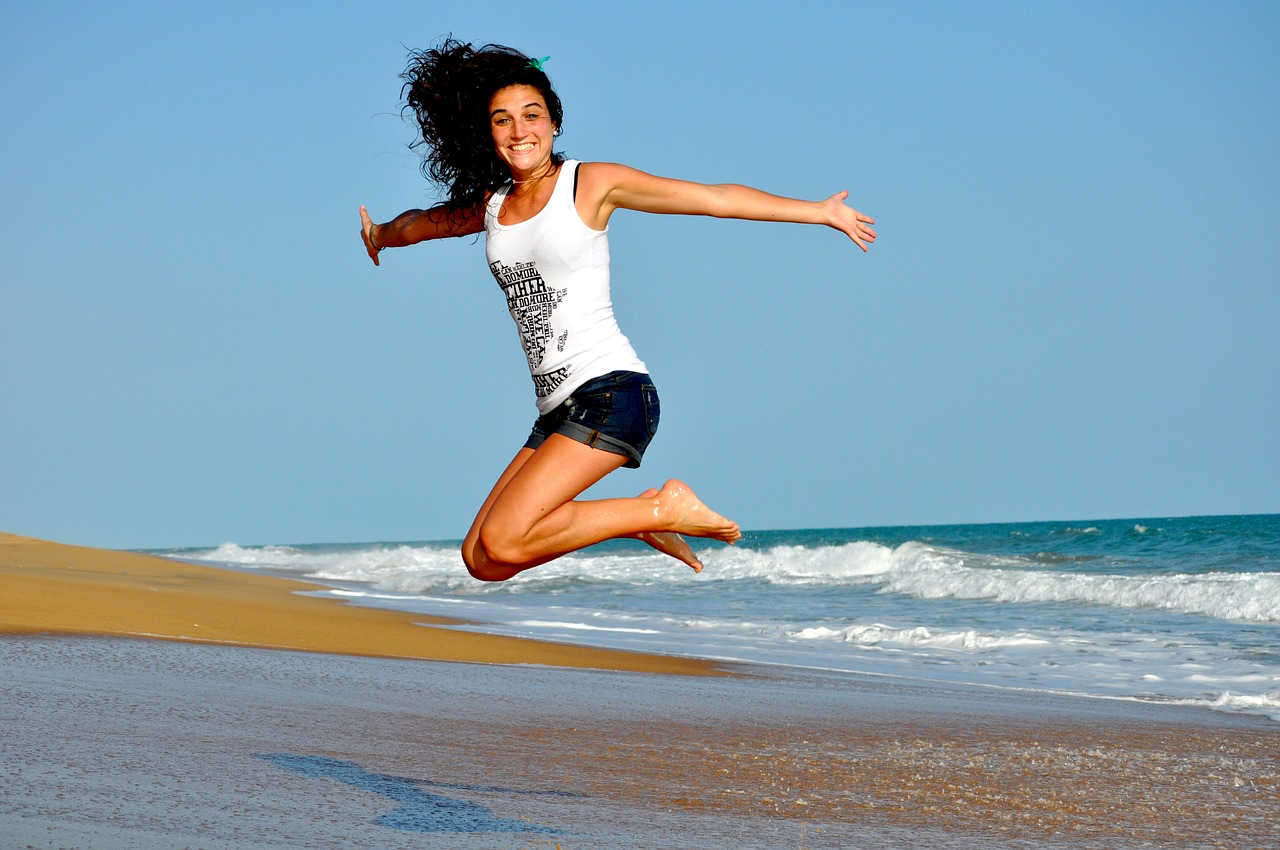 An image of a happy, exited woman jumping in the air at the beach. 