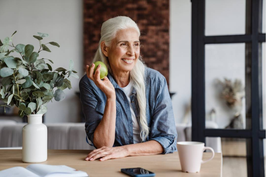 older white woman smiling with an apple thinking about blood clotting, bipolar disorder, antioxidant and anti inflammatory issues and how nac may help - The Good Stuff