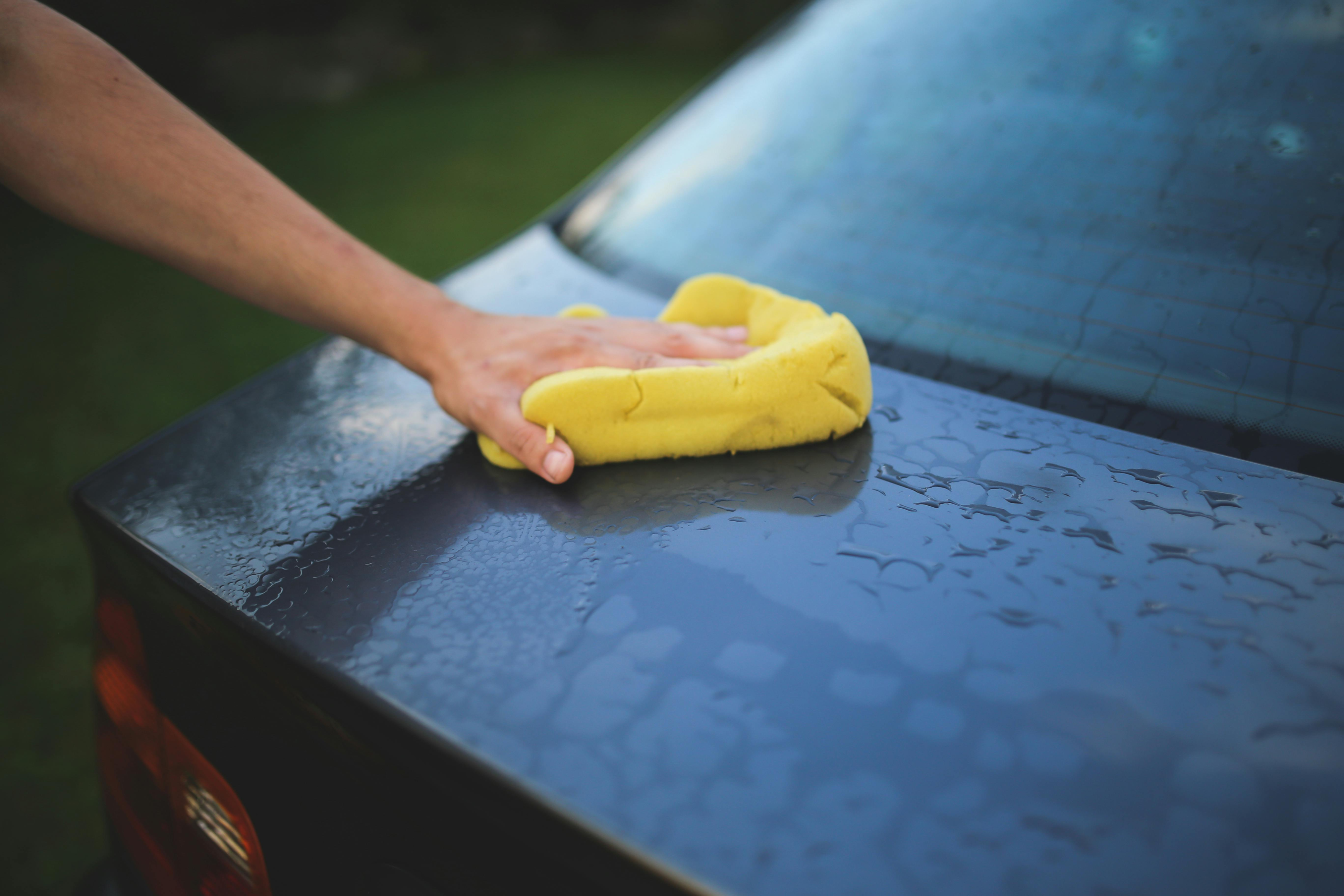Hand shown washing trunk of black car with yellow rag