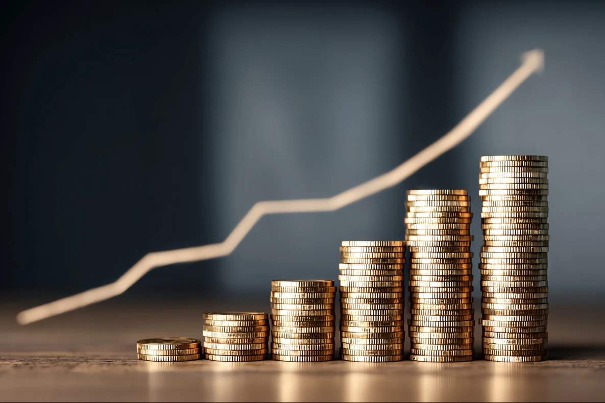 Stacks of coins increasing in height from left to right, with a rising line graph superimposed in the background.