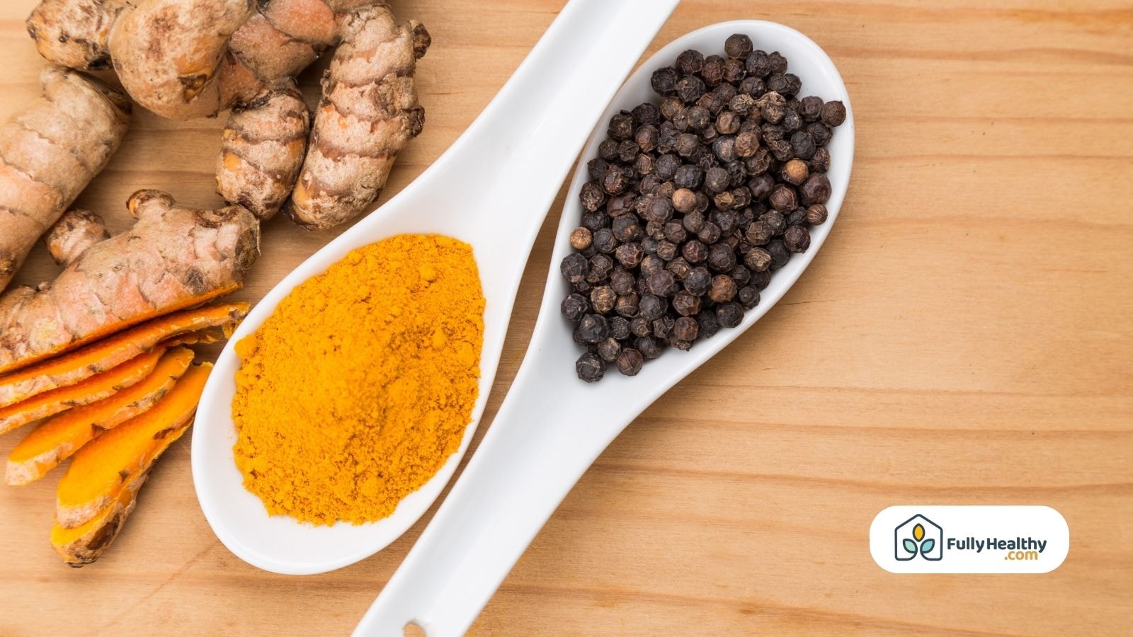 Fresh turmeric roots, ground turmeric powder, and whole black peppercorns in white ceramic spoons on a wooden surface