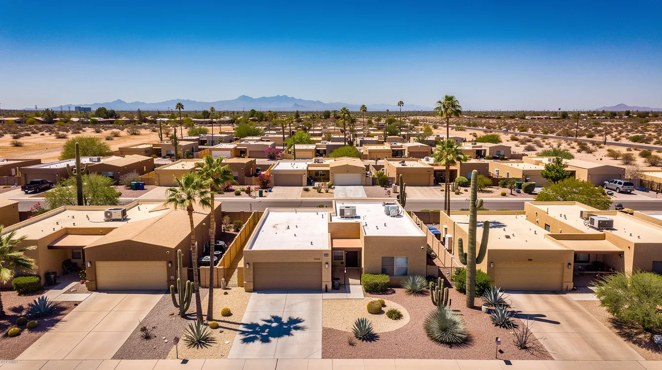 An aerial view captures a Phoenix, Arizona residential neighborhood featuring flat-roof homes and desert landscaping, all bathed in bright sunlight. The scene reflects the local architecture and environment, highlighting the unique charm of the area, where residents may rely on plumbing services for their essential plumbing needs.