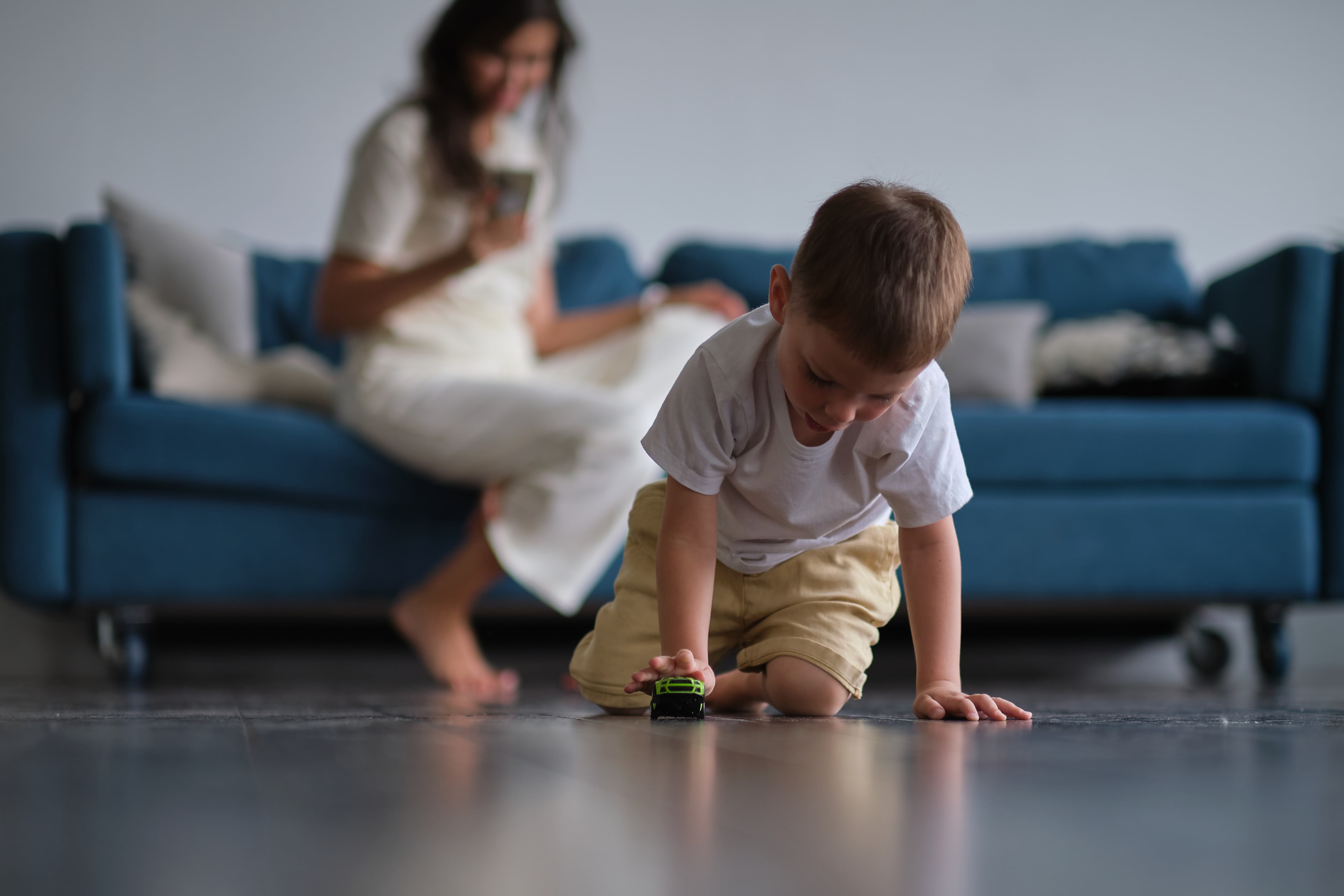 Image of young pretty little boy playing on the floor with car toys and drawing while his mother