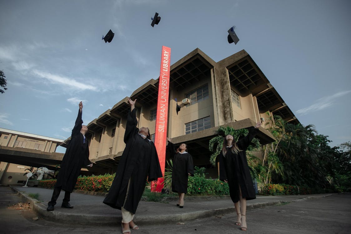 Silliman University graduates throwing caps in front of the university library