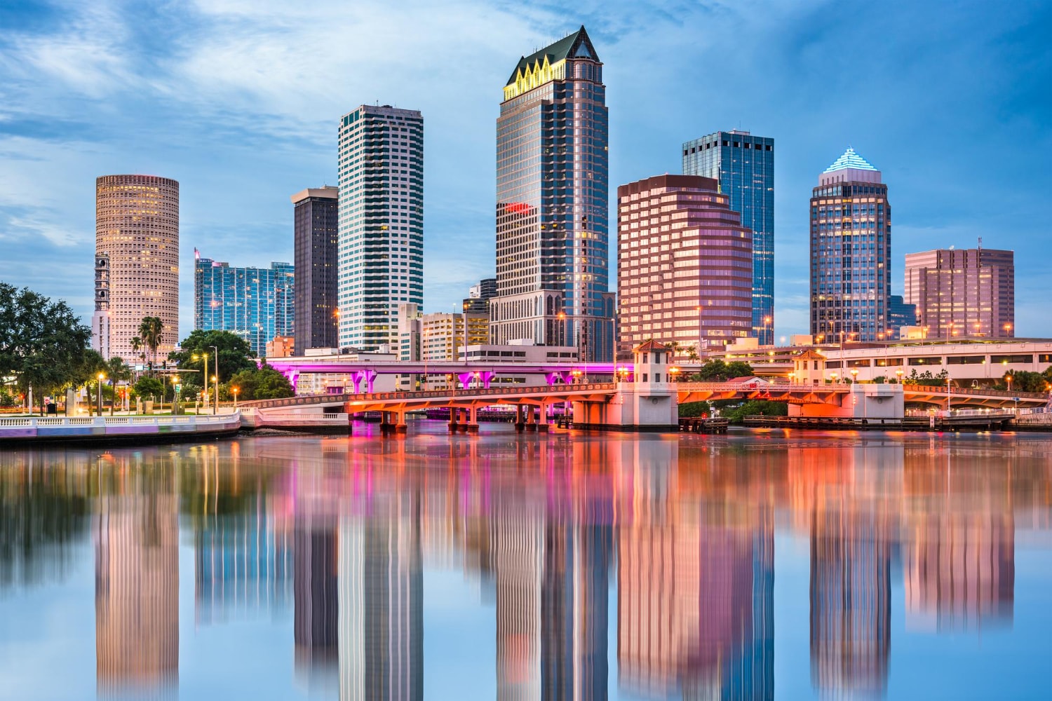 A colorful skyline of downtown Tampa with towering skyscrapers and a bridge reflecting on the calm river. This picturesque setting highlights the economic hub where business phone service in Tampa and local VoIP providers help businesses stay connected with reliable phone systems.