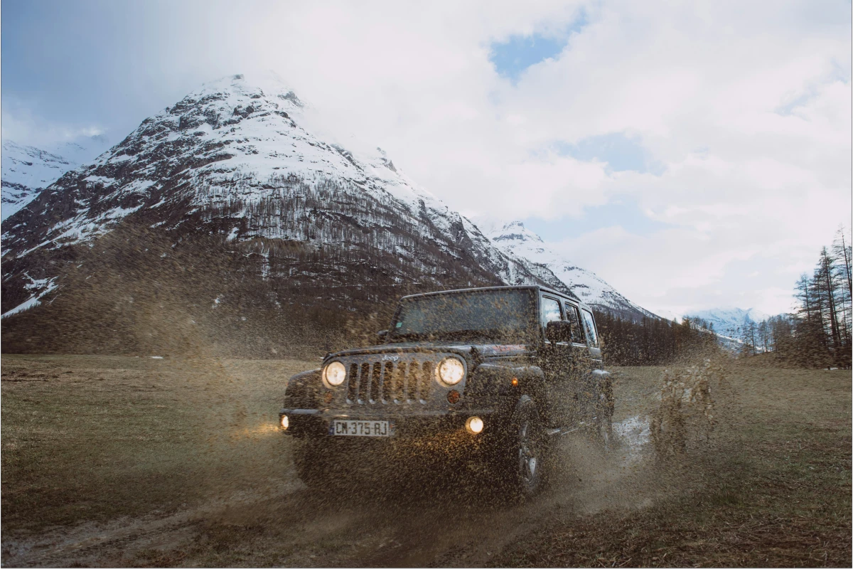Jeep 4x4 drives off-road through mud with snowy mountain in background