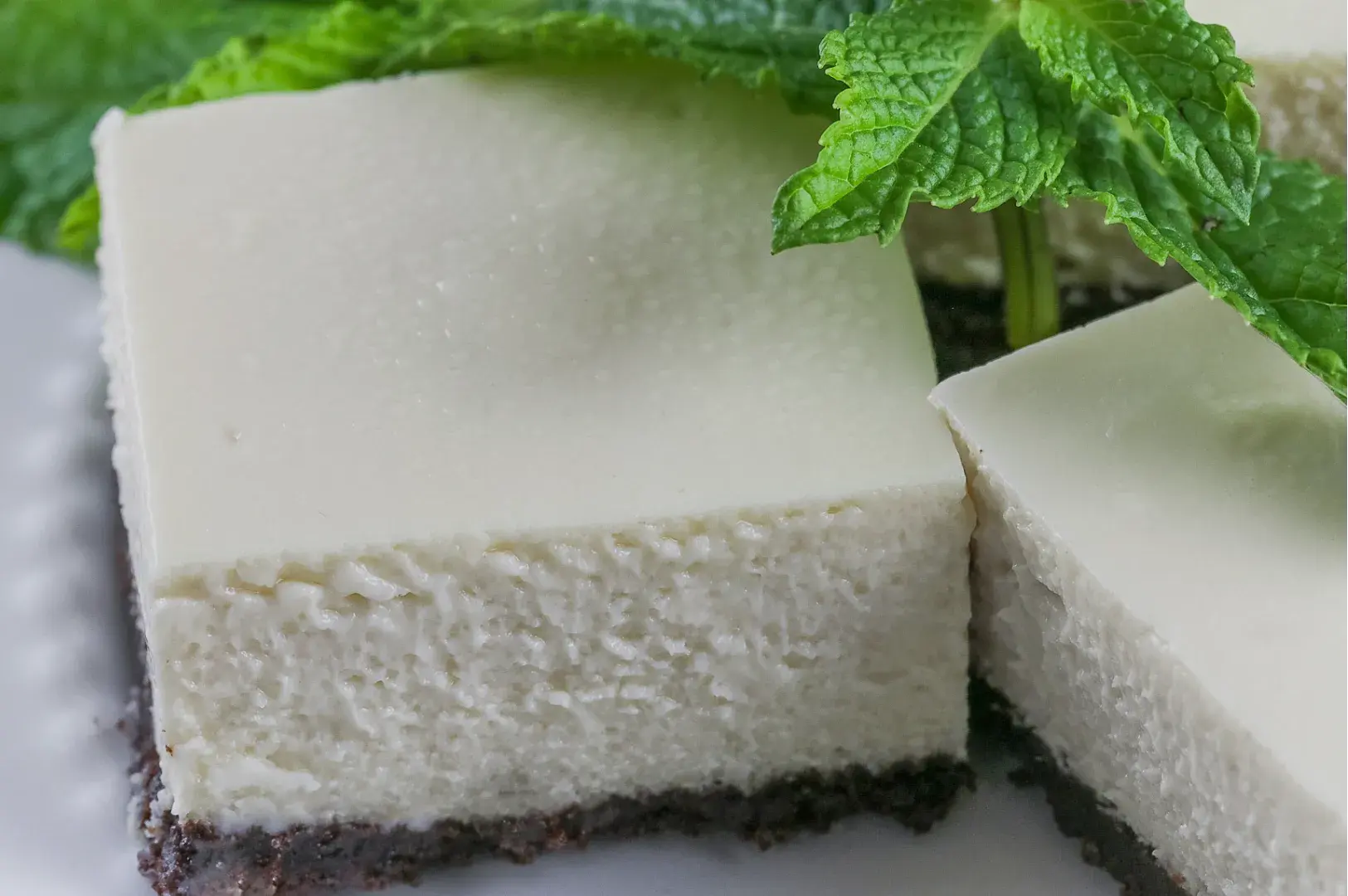 A close-up of a sliced piece of creamy cheesecake on a crust, garnished with fresh mint leaves.