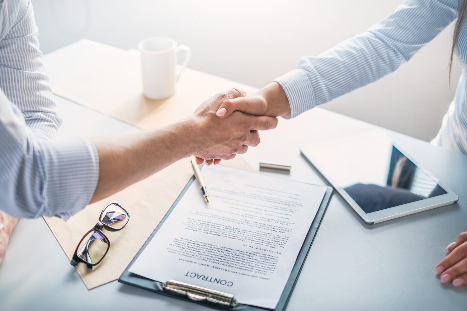 Two people shaking hands over a document on a desk.