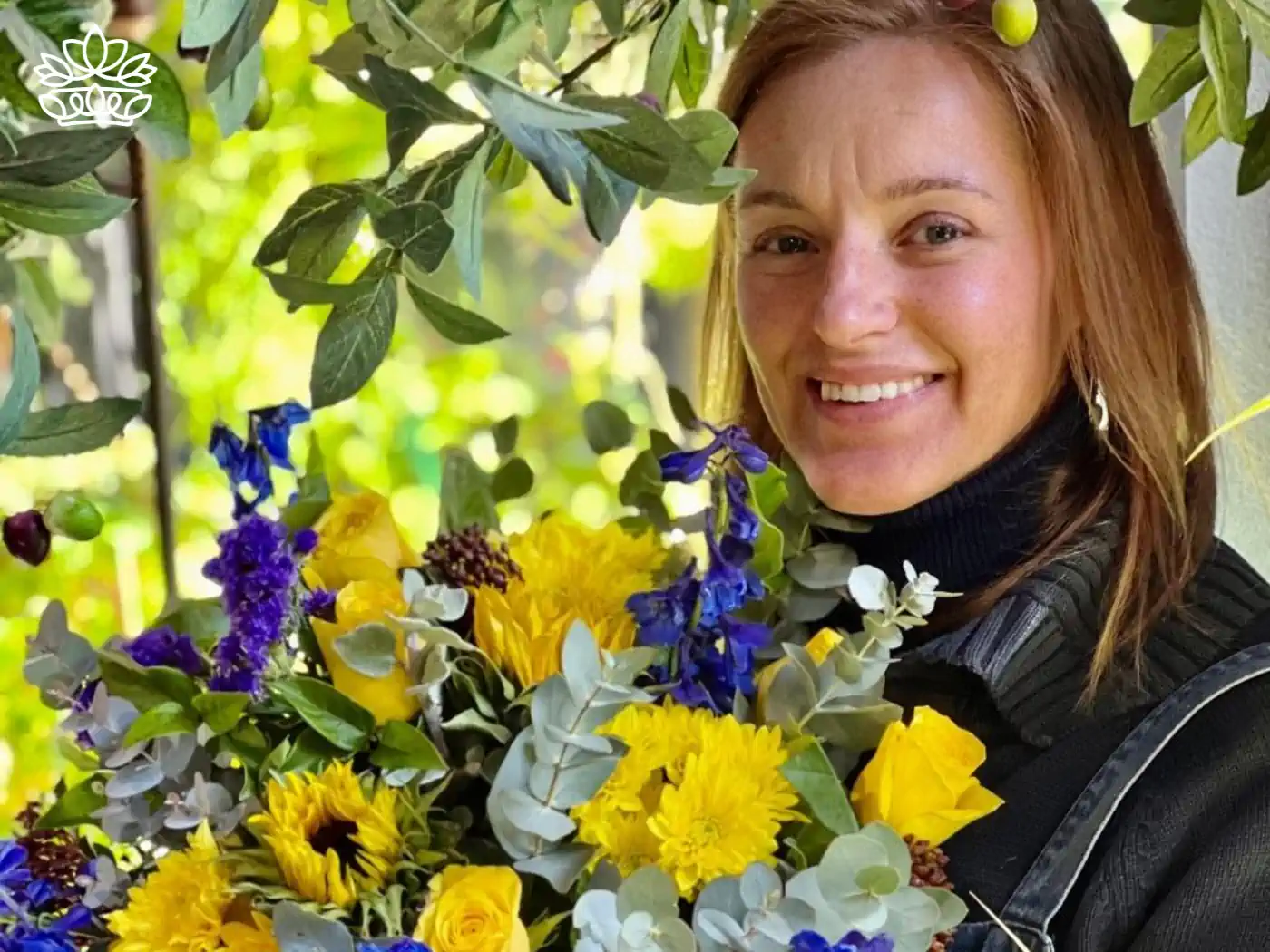 A smiling sa florist holds a luxurious bouquet featuring roses and other flowers, artfully arranged and vibrant in color, within a lush, green garden setting. This image highlights the beauty of flower delivery from a local flower shop. Fabulous Flowers and Gifts.
