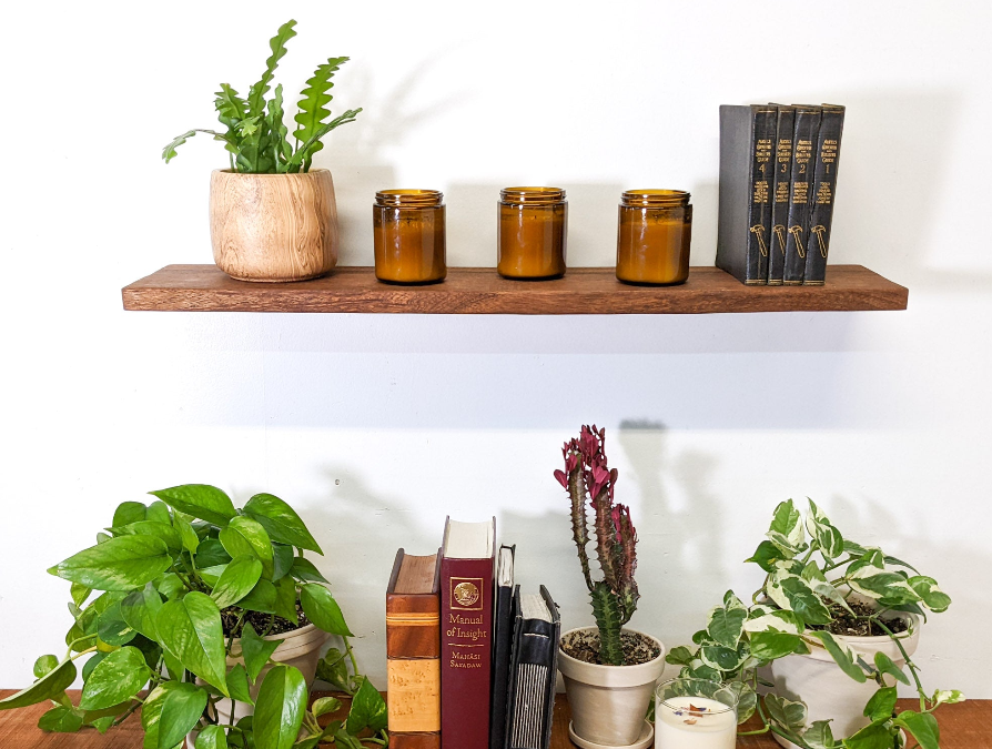 Two mahogany floating shelves are stacked one on top of the other. Various items are displayed on top including attractive plants, candles, and black books 