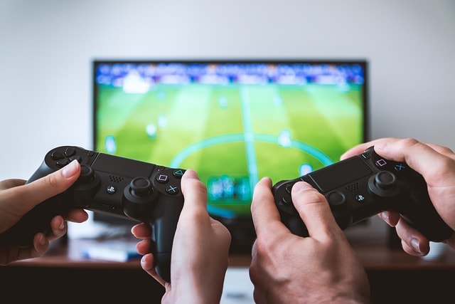 Two pairs of hands holding Playstation controllers while soccer game is on TV