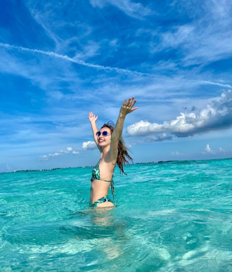 woman in a bikini standing in a turquoise sea with her arms in the air