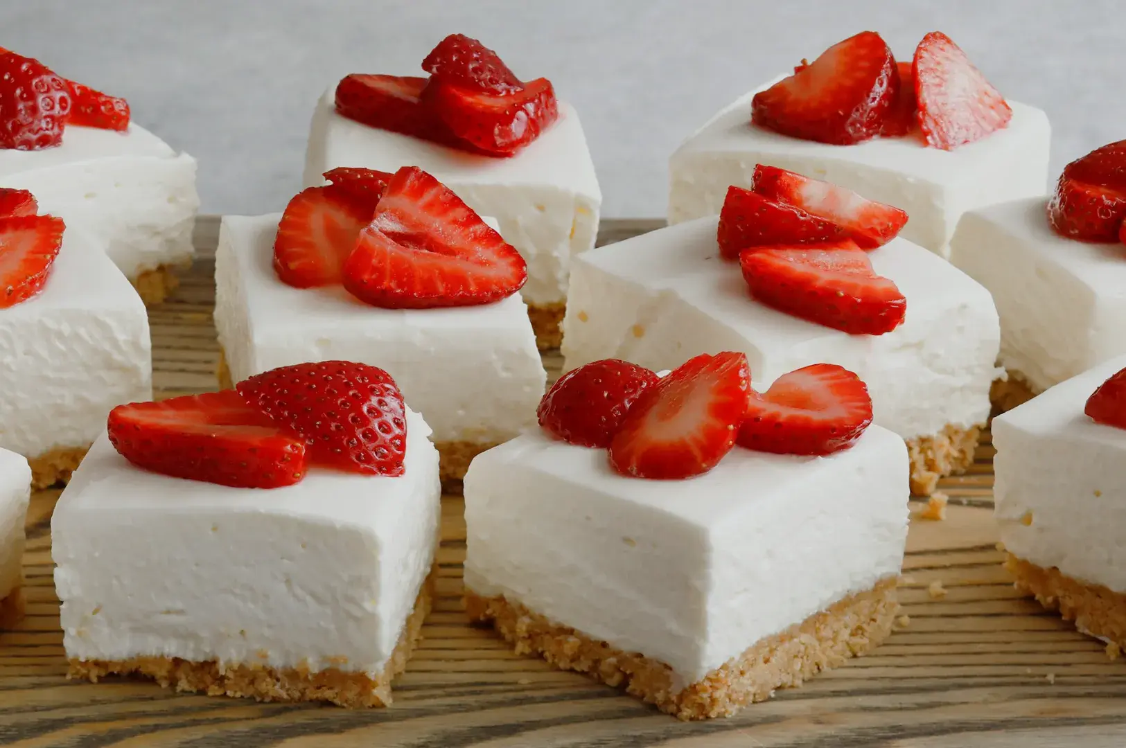 Slices of cheesecake topped with fresh strawberries on a wooden platter.