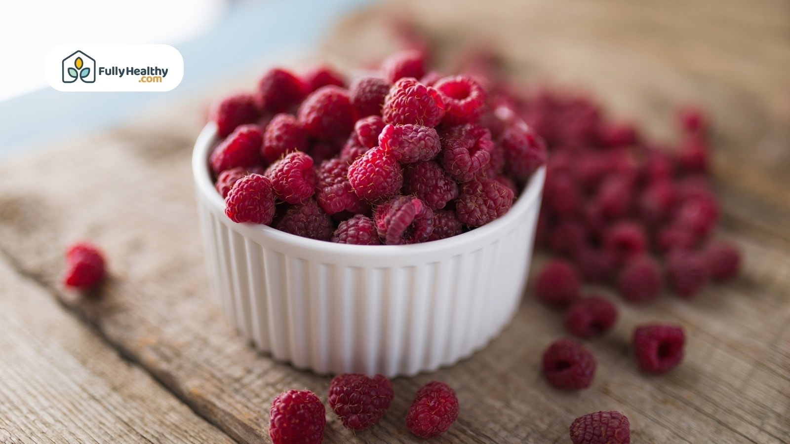White bowl overflowing with fresh raspberries on rustic wooden surface