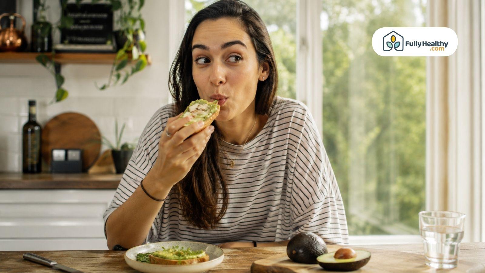 Woman tasting avocado toast in a bright kitchen.