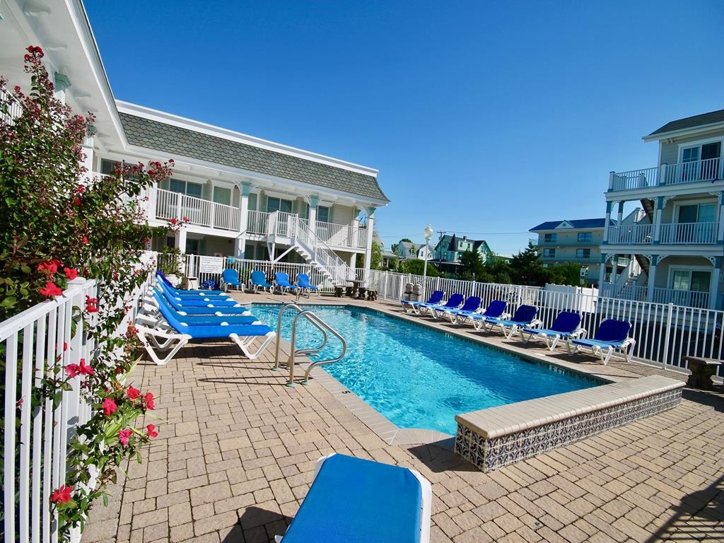 Heated outdoor pool with lounge chairs at Broadway Beach Condos Cape May, surrounded by white fencing and nearby Victorian homes.