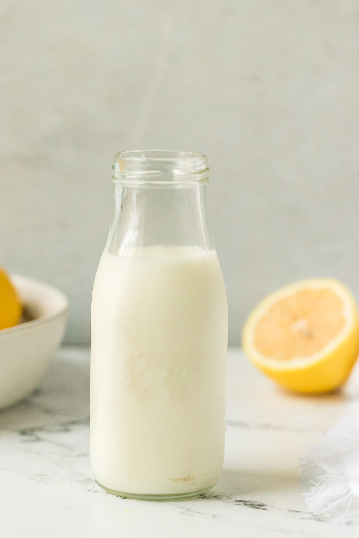 small glass milk jug of buttermilk with lemons in the background