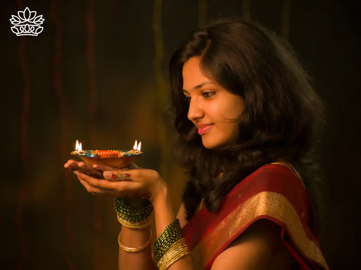 Young woman in a traditional saree holding a Diwali diya, her face illuminated by the gentle glow of the candlelight, symbolising peace and prosperity. Diwali. Delivered with Heart by Fabulous Flowers and Gifts.